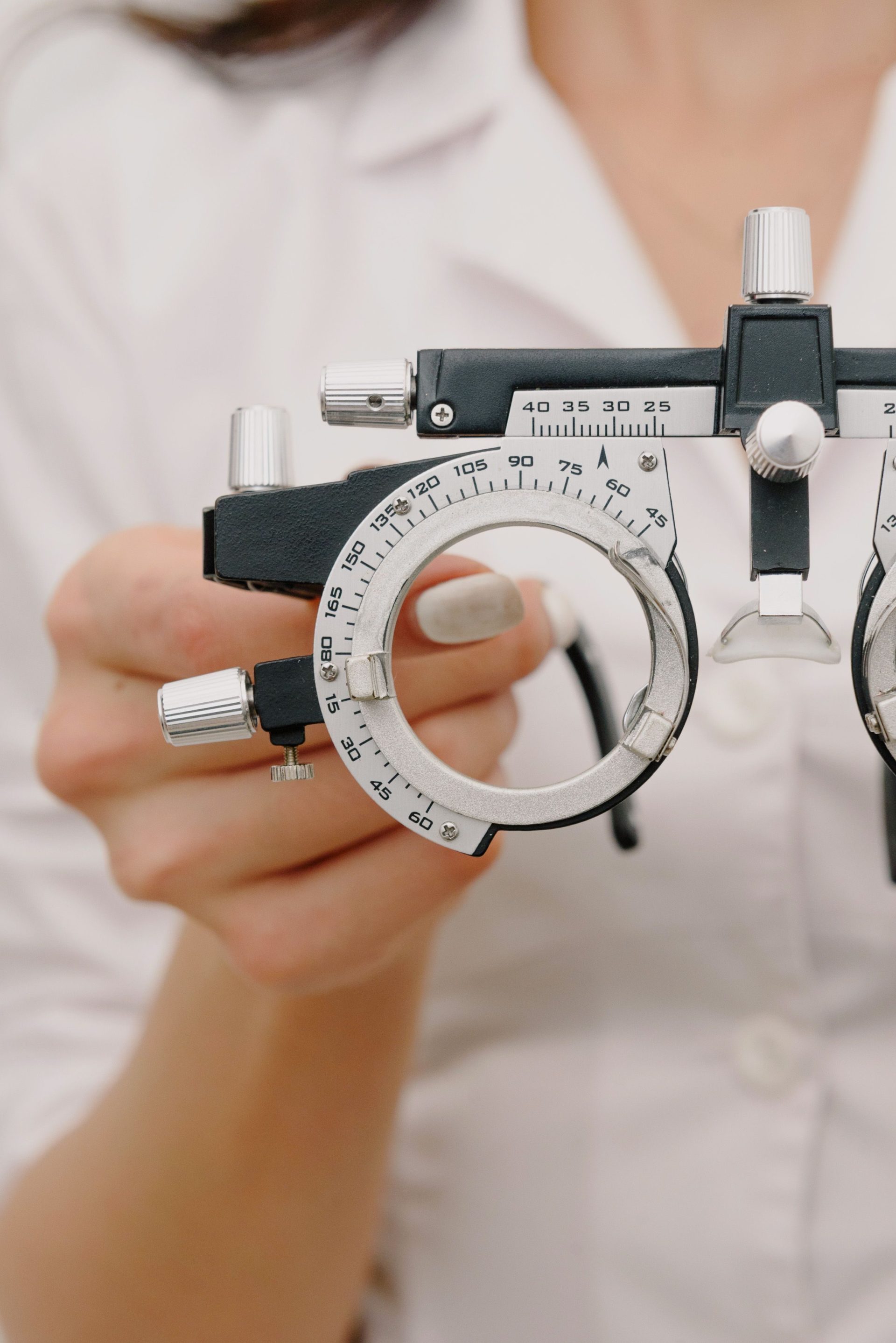 Crop anonymous female ophthalmologist in white medical robe showing modern trial frame while working in light optometry clinic